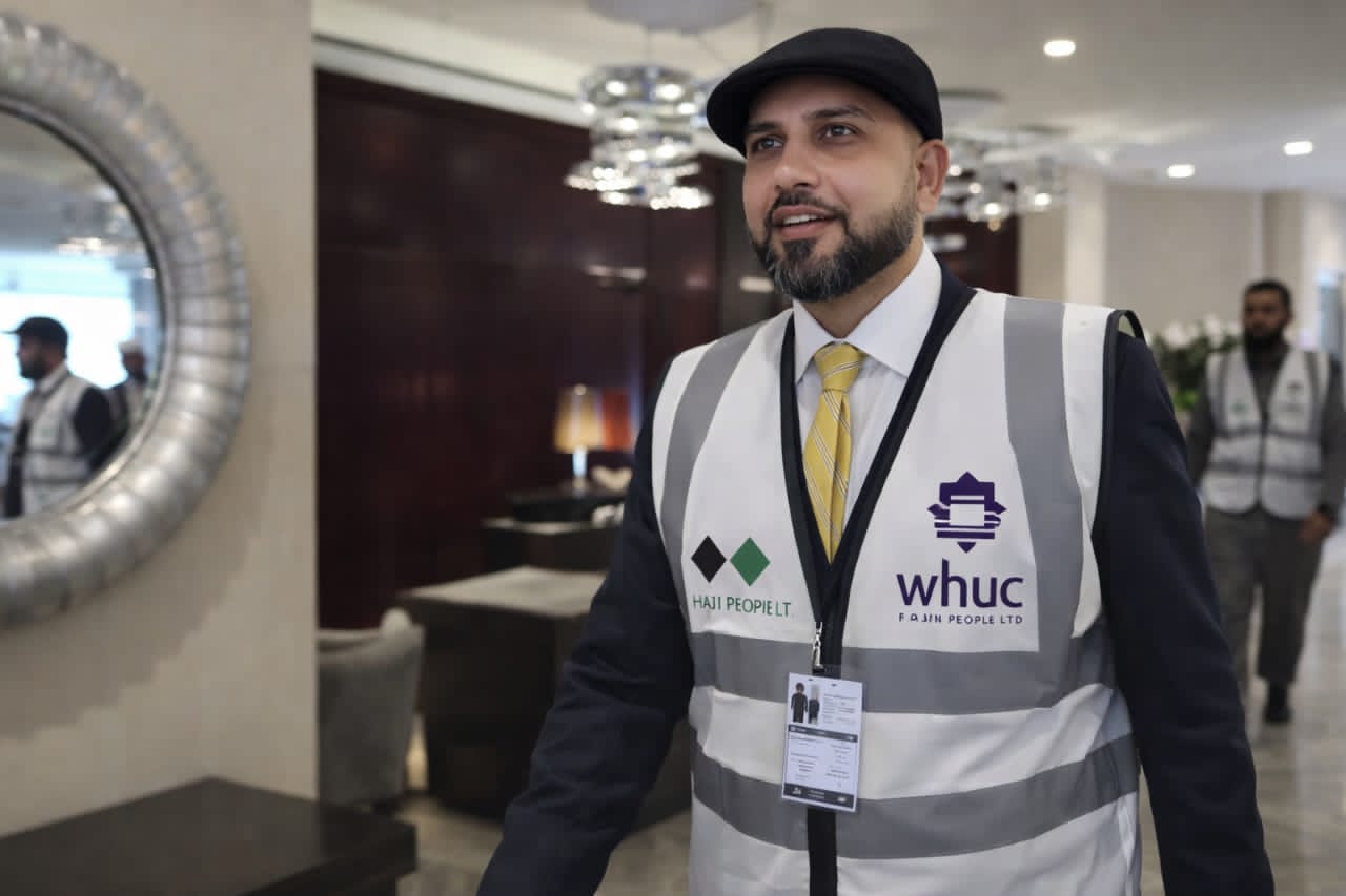 Mohsin Tutla wearing a Hajj People and WHUC Pilgrim Care high-visibility vest in a hotel lobby