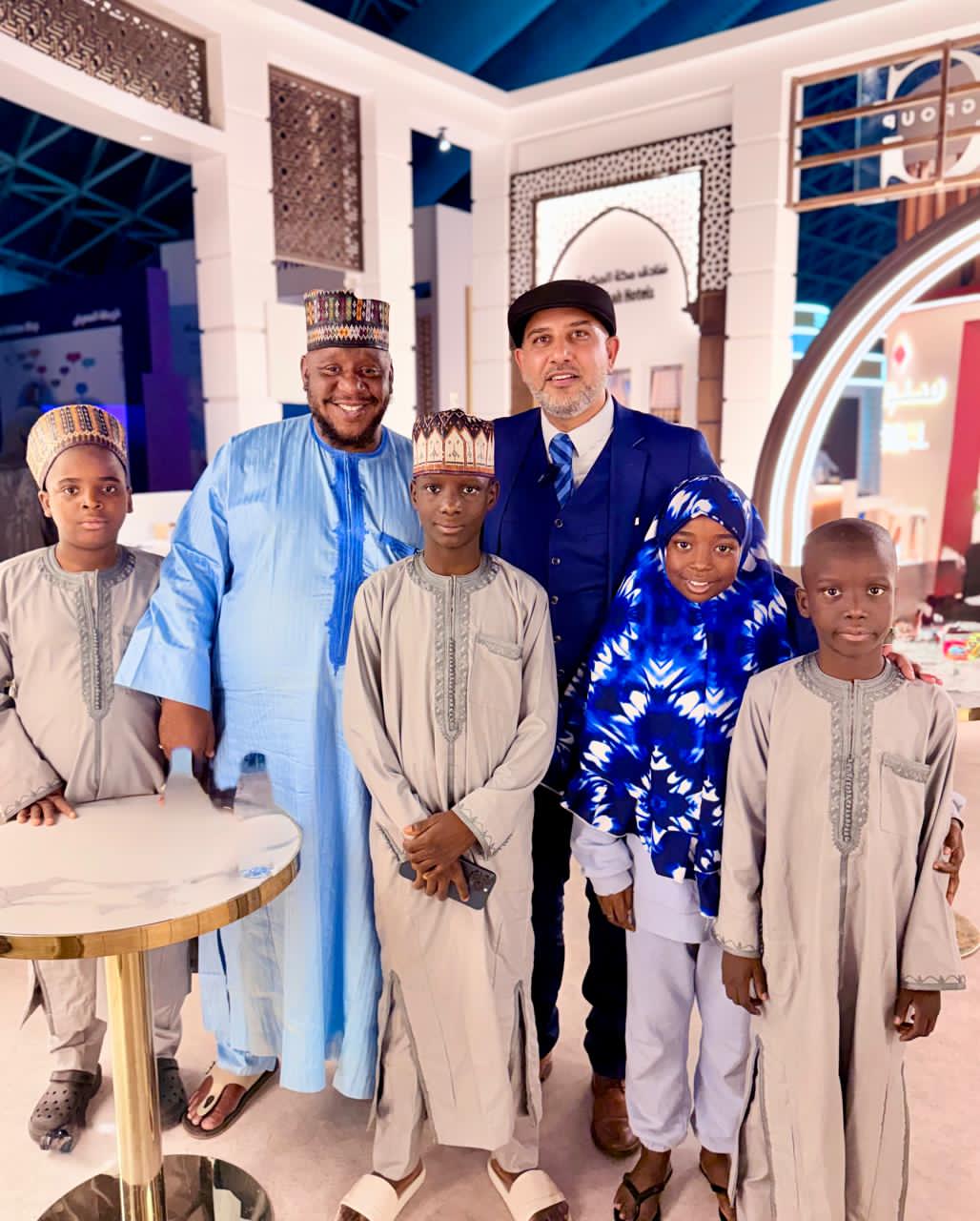 Mohsin Tutla with a man and children in traditional West African dress at an exhibition stand